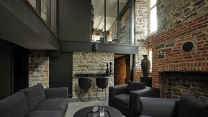 A modern living room with a stone wall, a fireplace, and a high ceiling. - Hôtel Maison du Fort (Québec City)