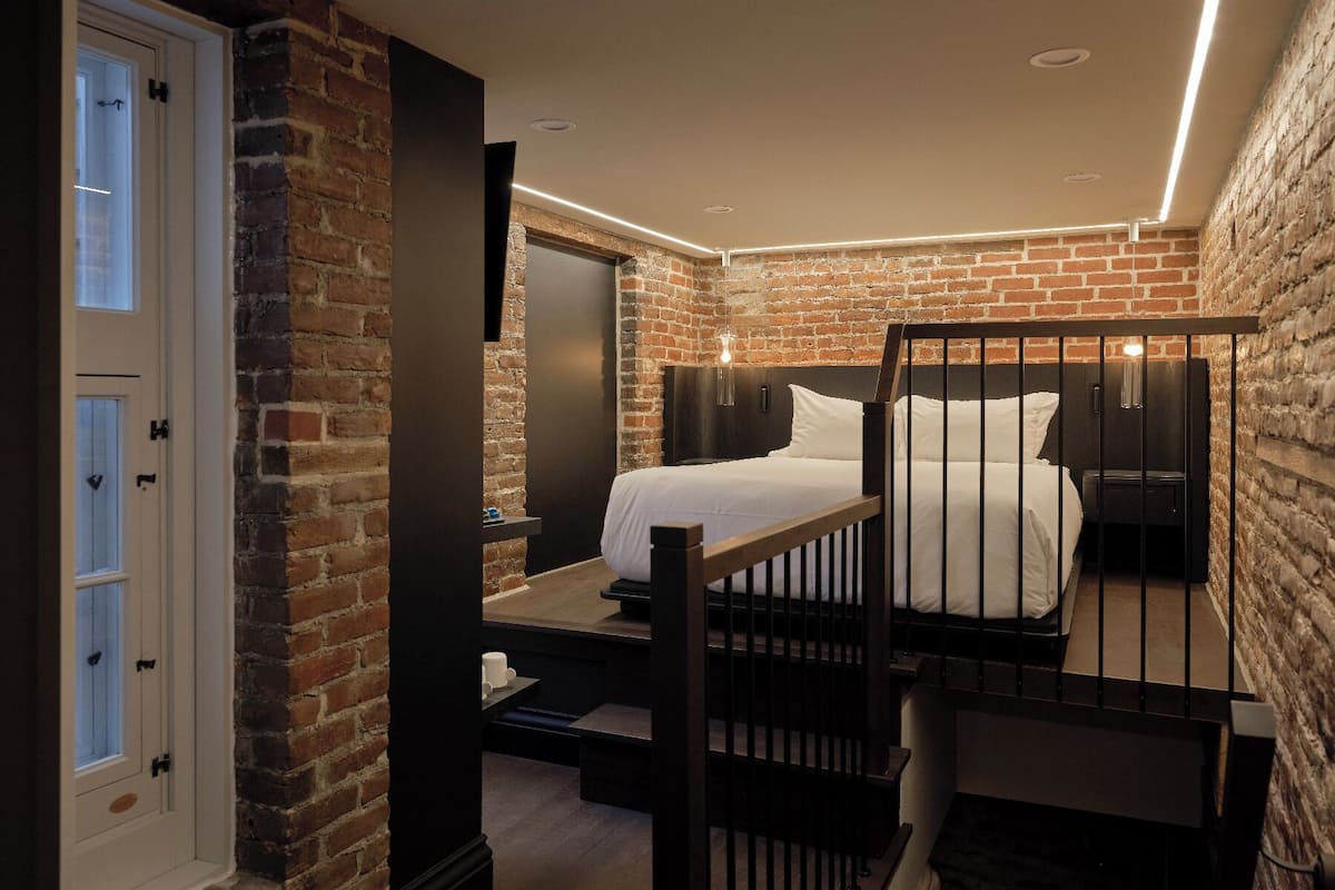 Ein Schlafzimmer mit Backsteinwand, einem Bett, einem Nachttisch und einer Tür mit Milchglasfenstern.