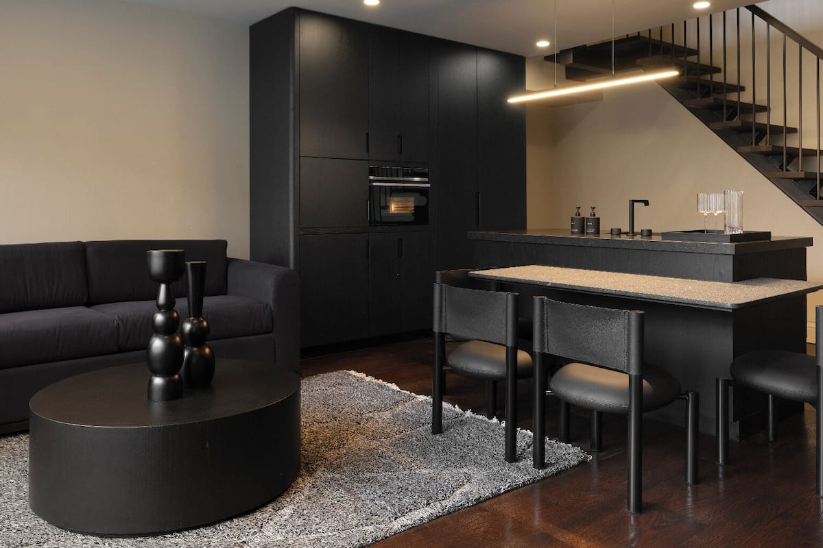 Ein modernes Wohnzimmer mit einem dunkelgrauen Sofa, einem runden Couchtisch und einer schlichten Essecke mit einer Bank und Stühlen.