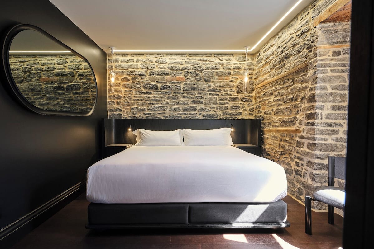 Ein modernes Schlafzimmer mit einer Steinwand, einem großen Bett, einem runden Spiegel und einem Nachttisch.
