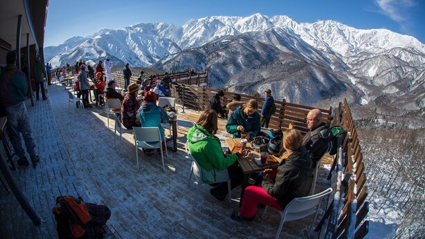 Area esterna con tavoli e sedie, coperta di neve e vista su una catena montuosa.