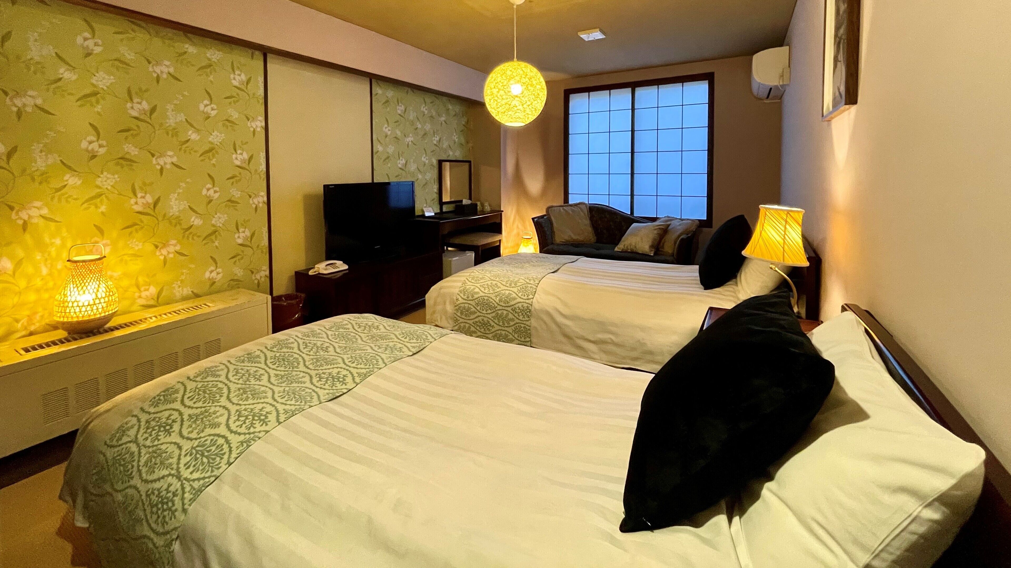 A hotel room with two beds, a television, a desk, and a window with a view.