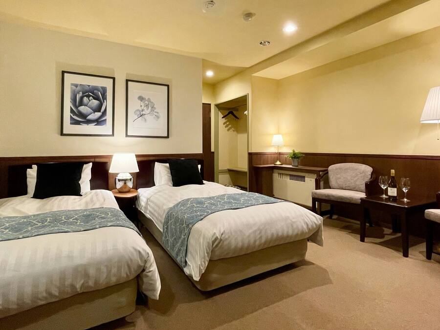 Habitación de hotel con dos camas, un escritorio, una silla, una lámpara y dos cuadros en la pared.