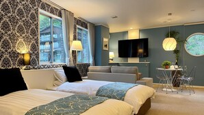 Camera d'albergo con due letti, una TV, un tavolino con sedie e una finestra con tende.
