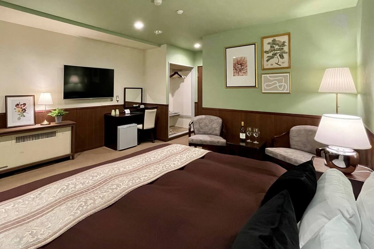 A hotel room with a large bed, a desk with a computer, a television, and a seating area with two chairs.