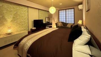 A bedroom with a bed, a desk, a chair, a television, and a window.
