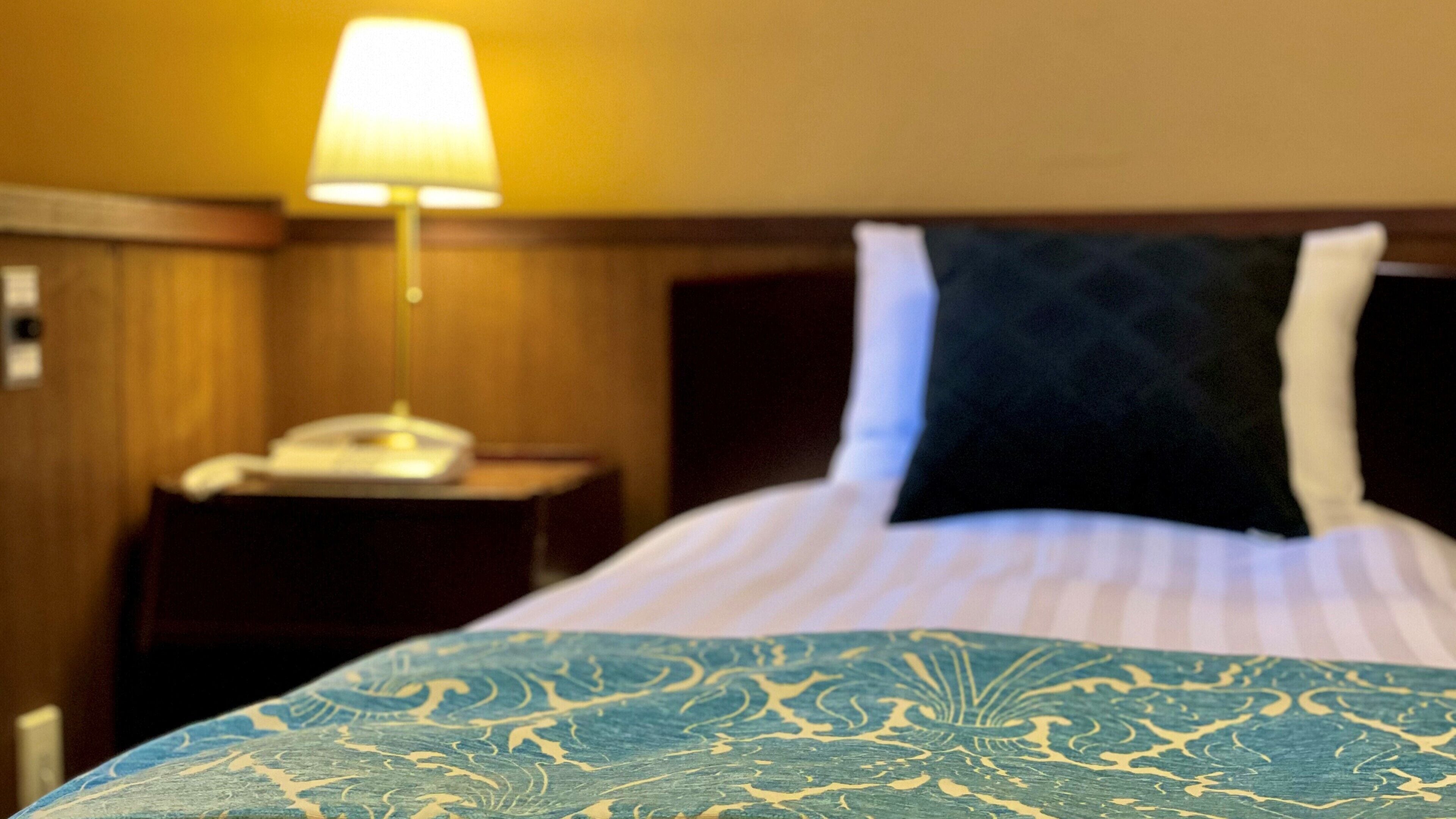 Una habitación de hotel con una cama, una lámpara de noche y un teléfono en la mesita de noche.