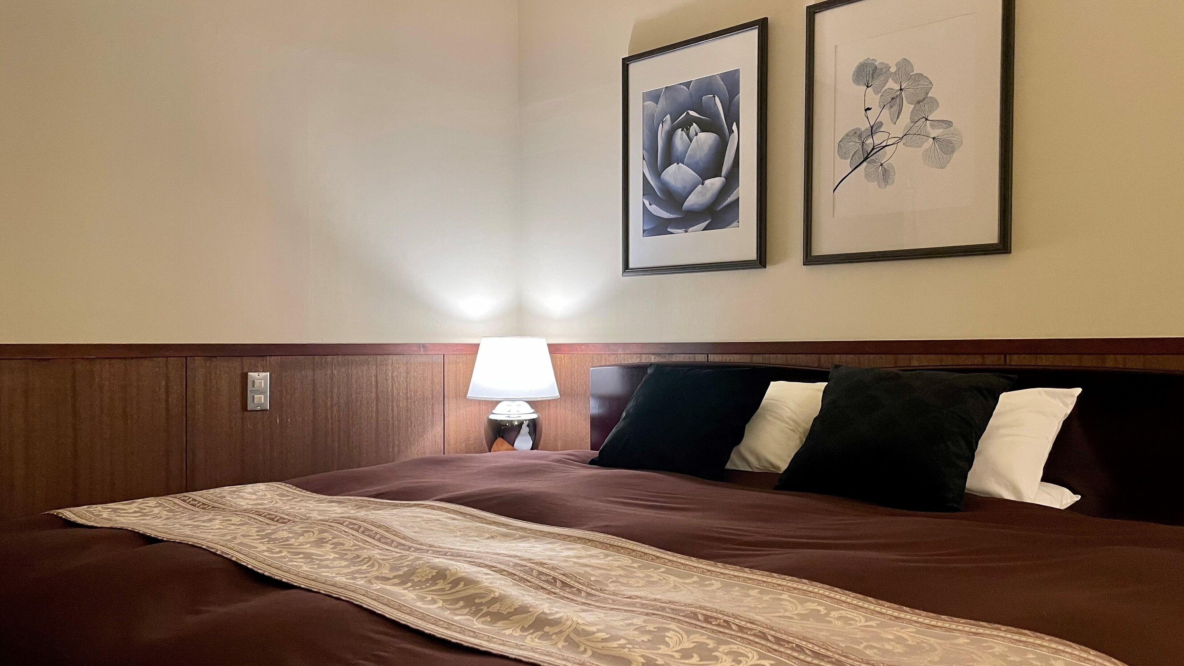 A hotel room with a large bed, a nightstand with a lamp, and two framed artworks on the wall.