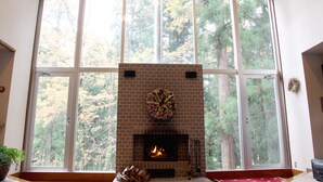 Un caminetto con rivestimento in mattoni e una ghirlanda decorativa sopra, in una stanza con ampie finestre che si affacciano su alberi.