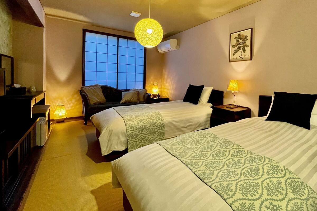 A hotel room with two beds, a sofa, a desk, and a large window.