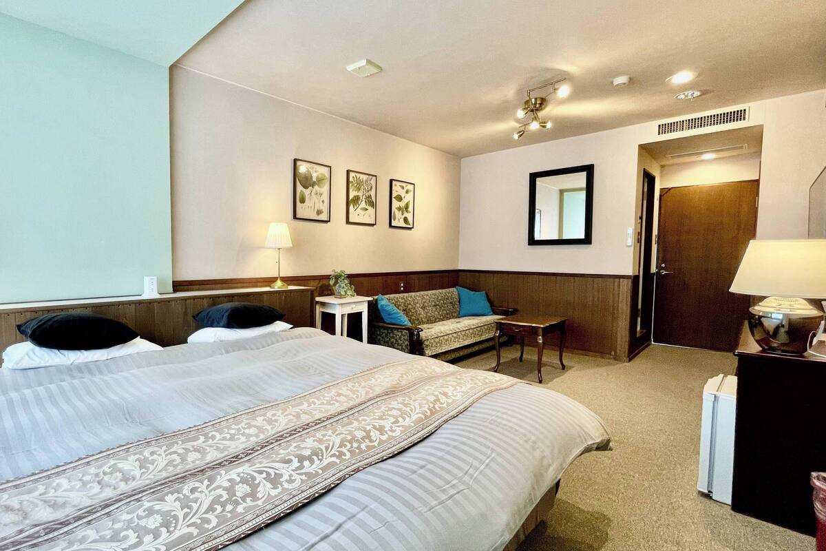 A hotel room with a large bed, a sofa, a small table, and a mirror.