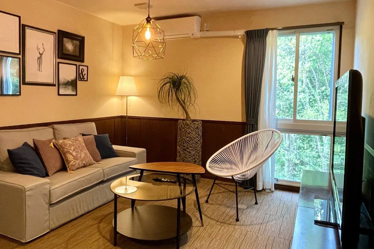 A living room with a sofa, a small table, a chair, a lamp, and a TV.