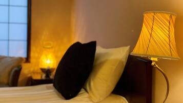 A bed with white linens, a black pillow, and a lamp with a yellow shade.