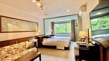 Quarto de hotel com cama, sofá, escrivaninha, televisão e janela com vista para o verde.