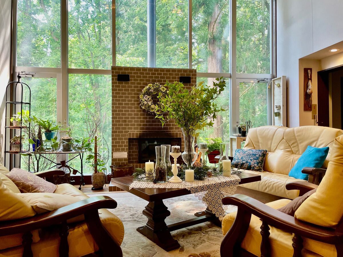 Un salon chaleureux avec une cheminée, des canapés en cuir et une grande fenêtre donnant sur une forêt.