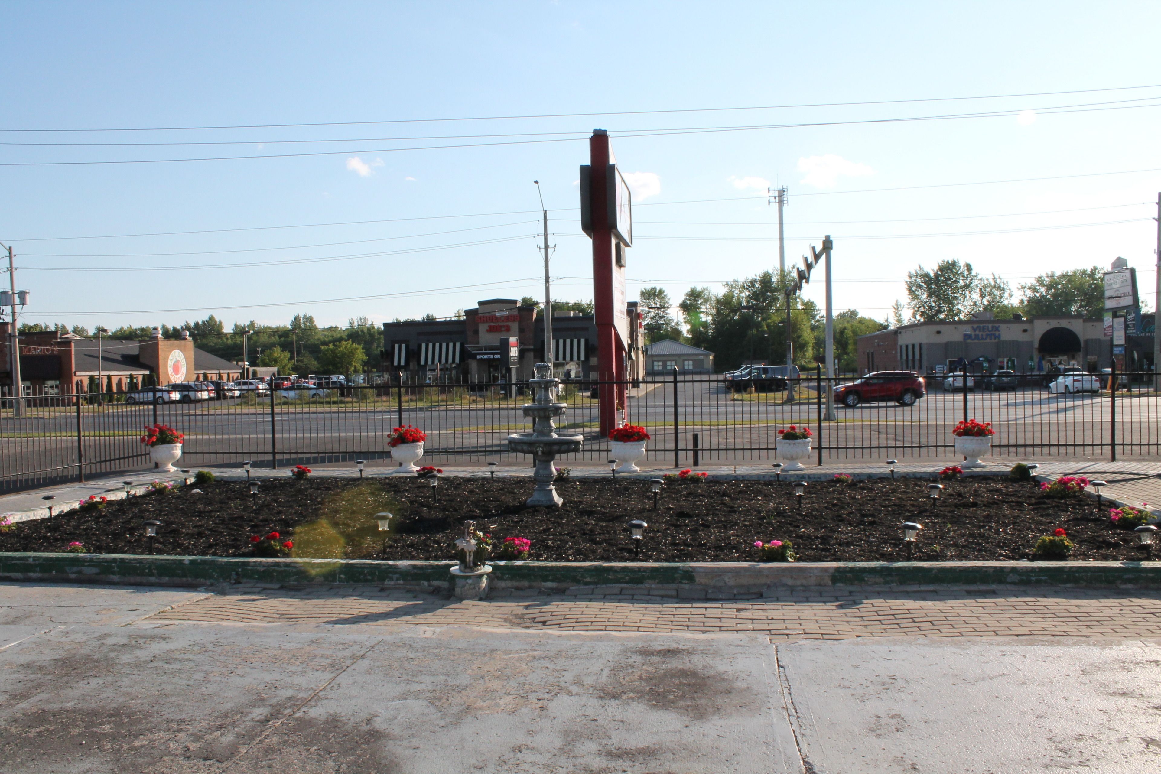 A parking lot with a fountain, a fence, and a building in the background.