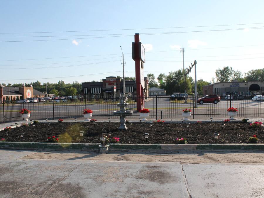 A parking lot with a fountain, a fence, and a building in the background.