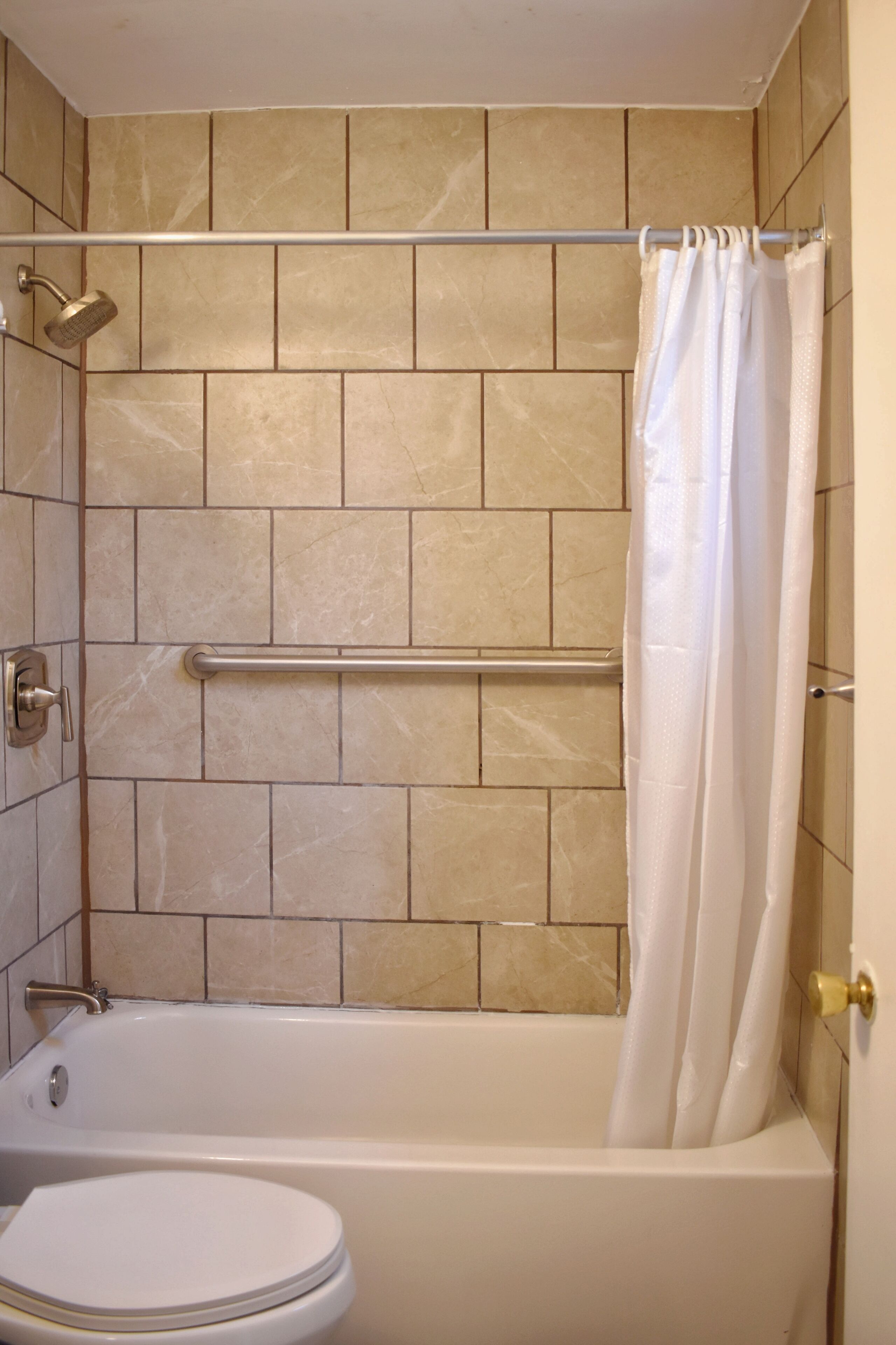 Un baño con bañera, inodoro y zona de ducha con barra de apoyo.
