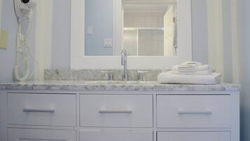 Une salle de bain dotée d’un comptoir en marbre, d’un lavabo avec un robinet moderne, d’un miroir au-dessus du lavabo et d’un sèche-cheveux fixé au mur.