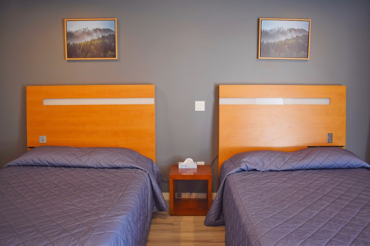 Dos camas individuales con cabeceros de madera, una mesita de noche de madera entre ellas y un marco de foto en la pared sobre cada cama.