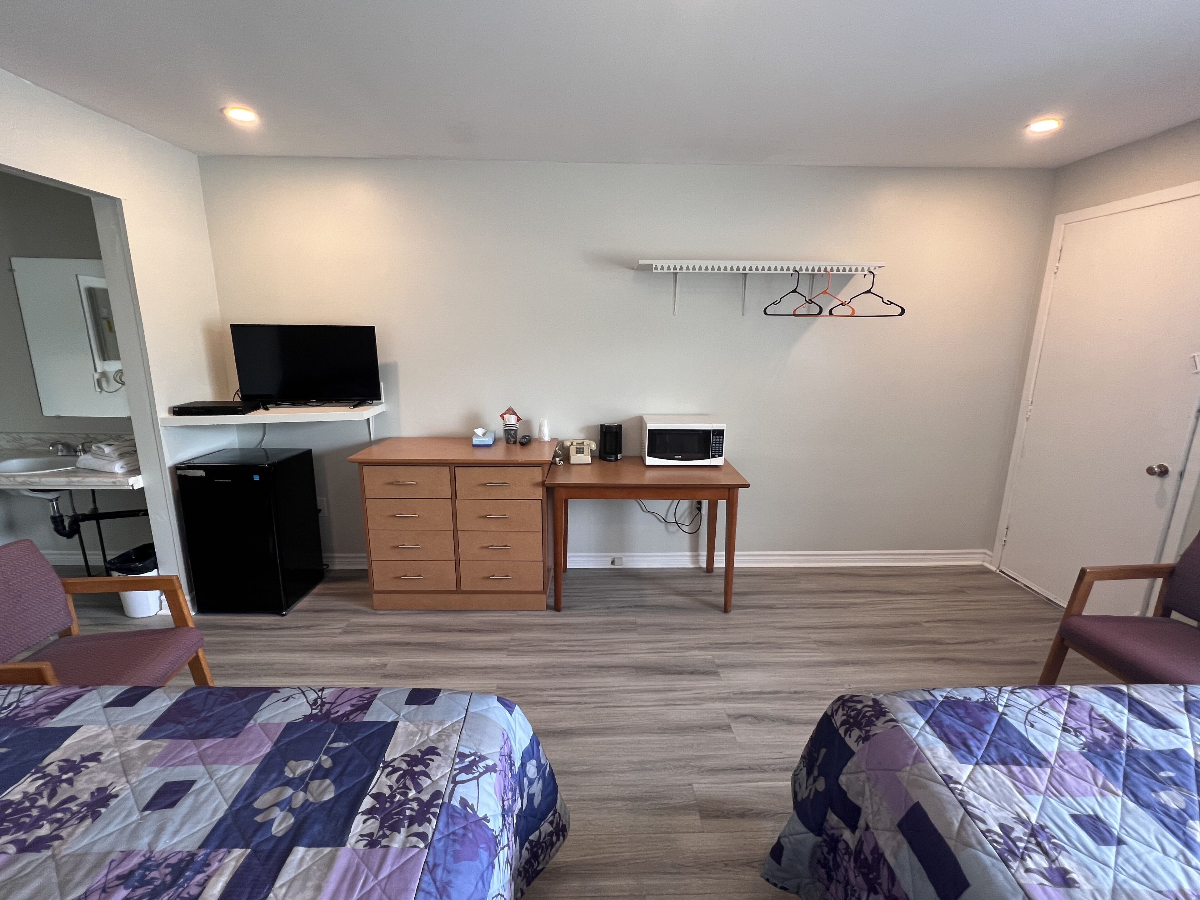 Habitación de hotel con dos camas, un escritorio con microondas, televisor, armario y un estante pequeño con perchas.