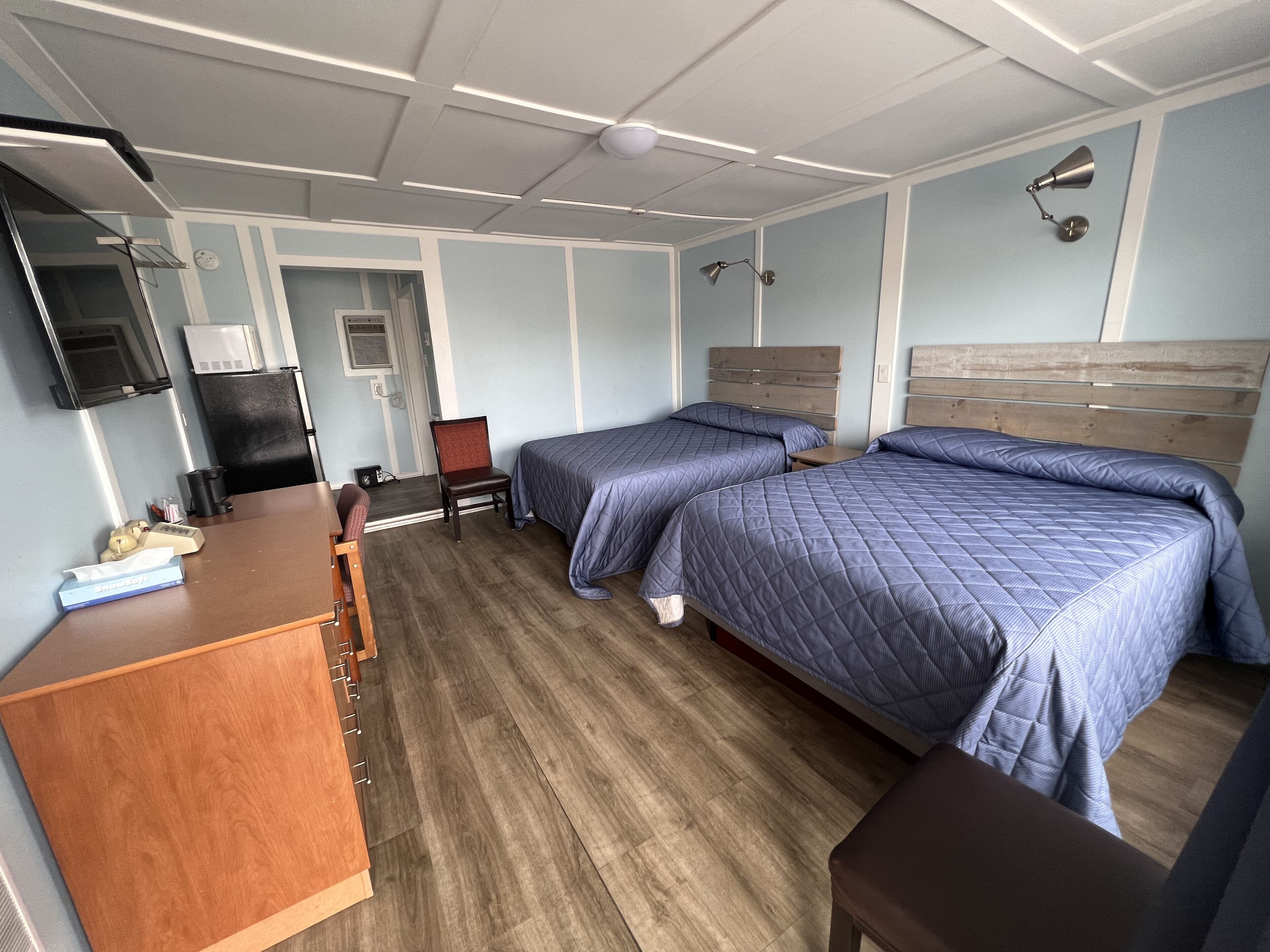 A hotel room with two beds, a desk, a chair, a TV, and a wardrobe.