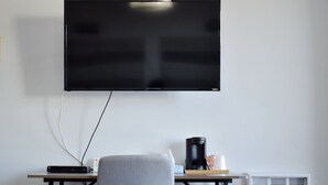 A room with a flat-screen TV mounted on the wall, a desk with a chair, a coffee maker, and a vent. - Elect Inn 5 (Cornwall)