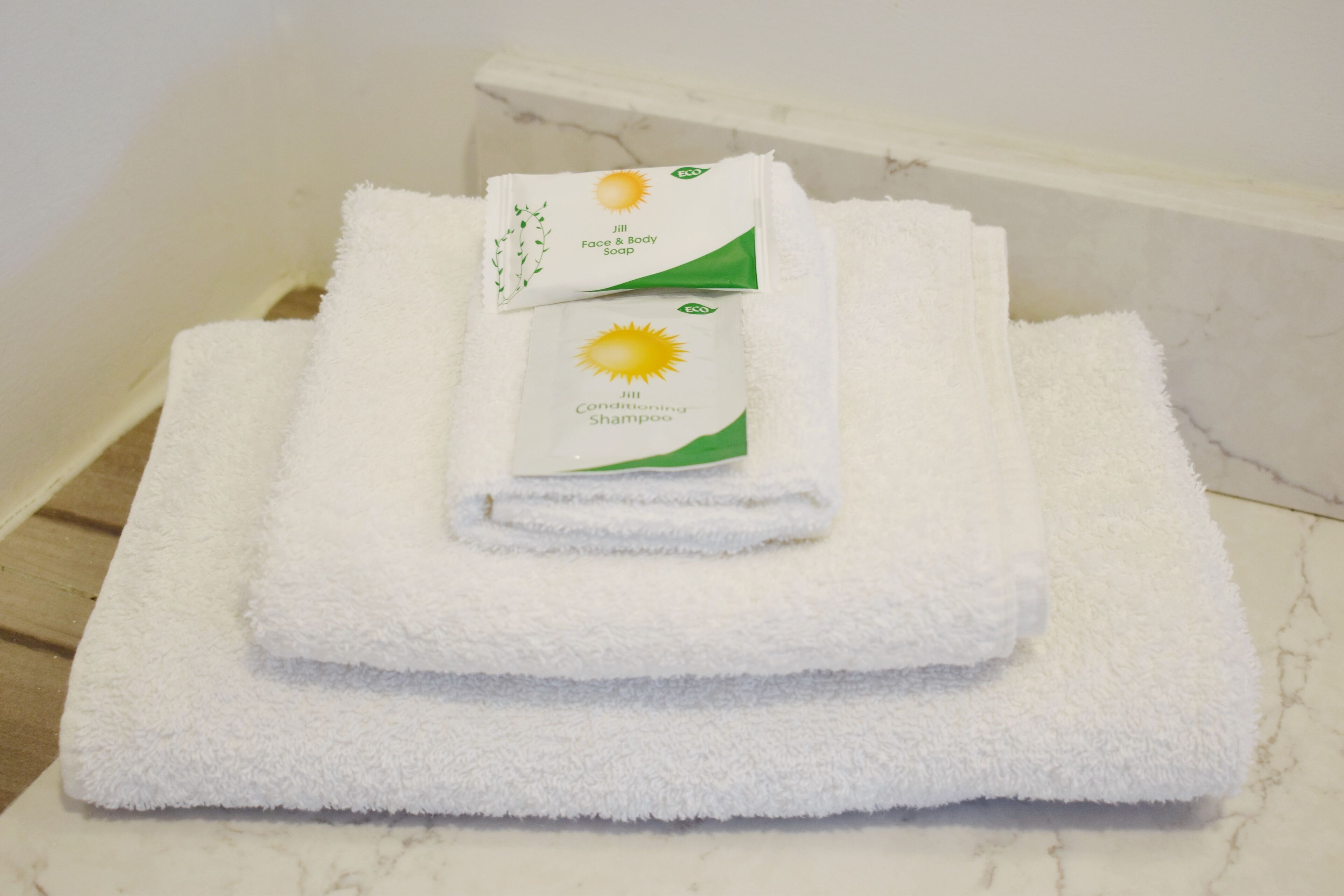 A set of white towels and a bottle of JILL Conditioning Shampoo on a marble surface.
