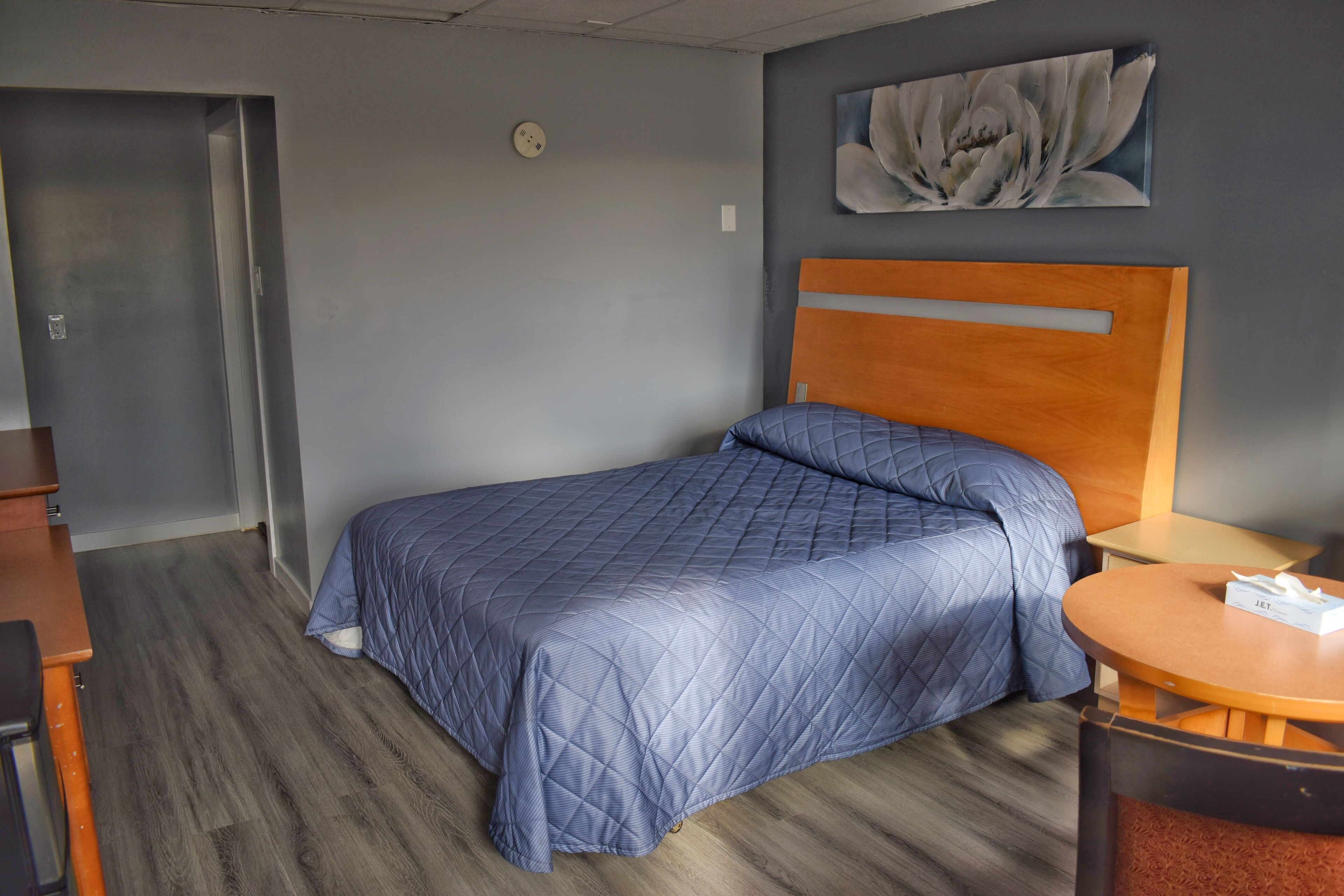 Une chambre d’hôtel avec un lit, une tête de lit en bois, une table ronde et un tableau au mur.