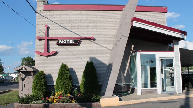 A motel with a prominent anchor sign, a small entrance with a glass door, and a brick planter with flowers. - Elect Inn 5 (Cornwall)