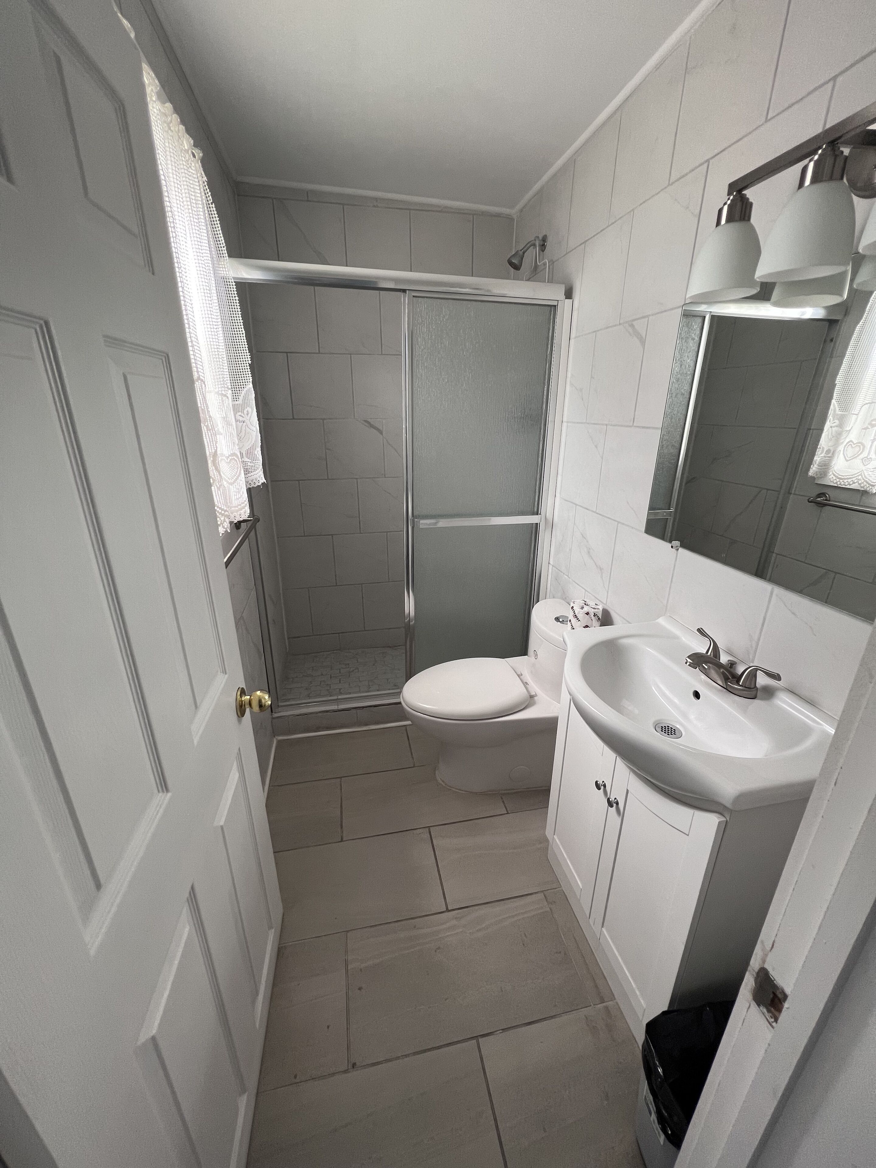 Baño con inodoro, lavabo, ducha y una puerta con una toalla colgada.