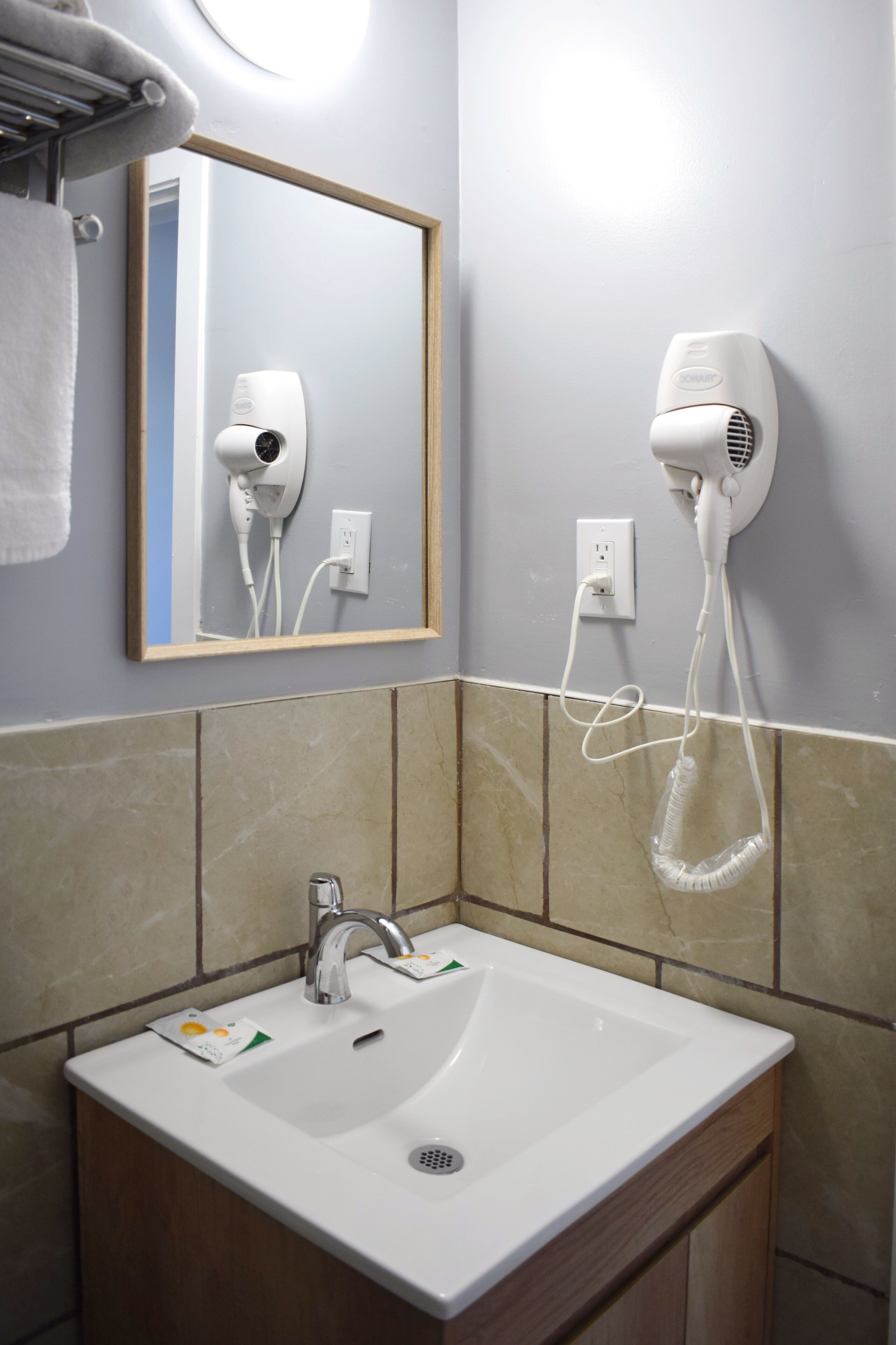 A bathroom with a sink, mirror, hair dryer, and towel rack.