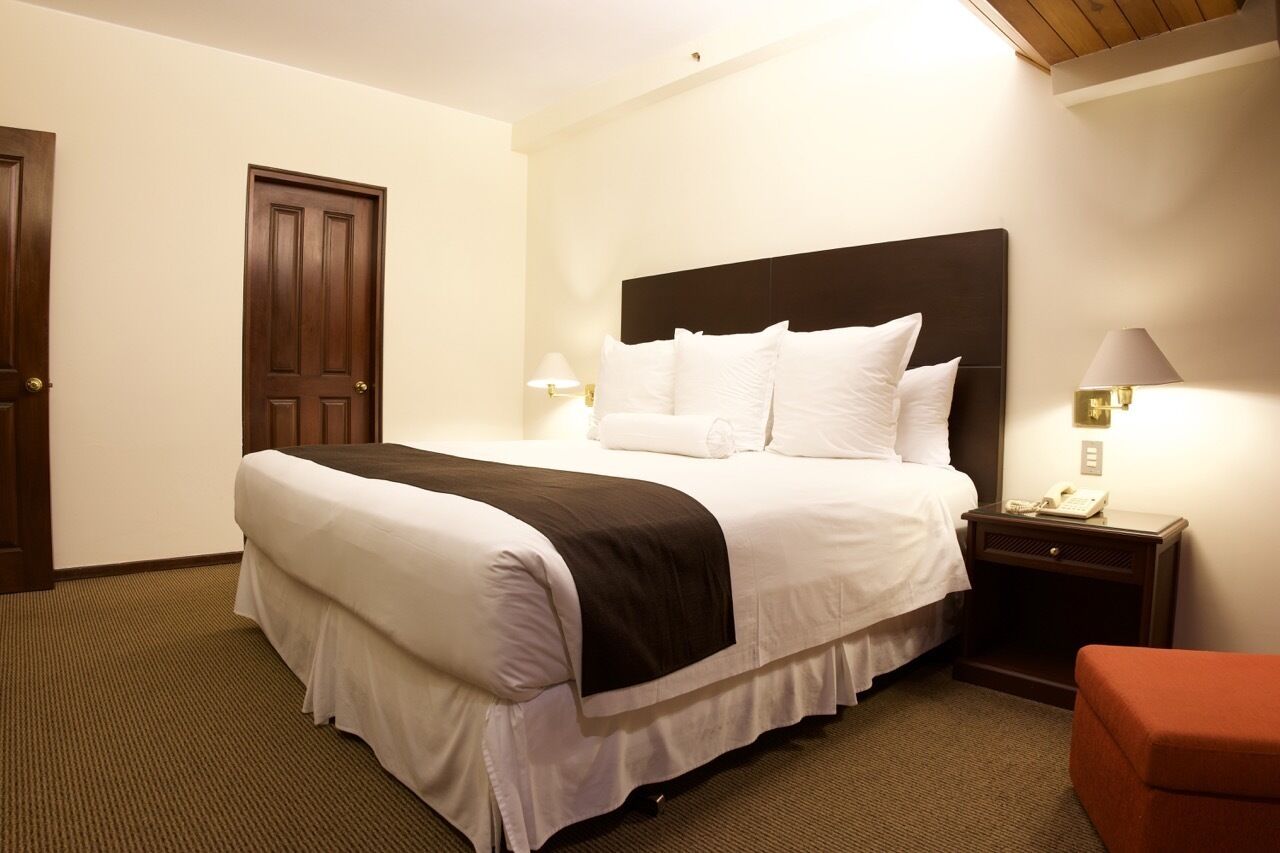 A hotel room with a large bed, a nightstand with a lamp, and a telephone.