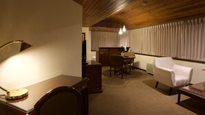 A hotel room with a wooden ceiling, a desk with a lamp, a chair, a dining table with chairs, and a large window with curtains. - J&A Classic Hotel (Lima)