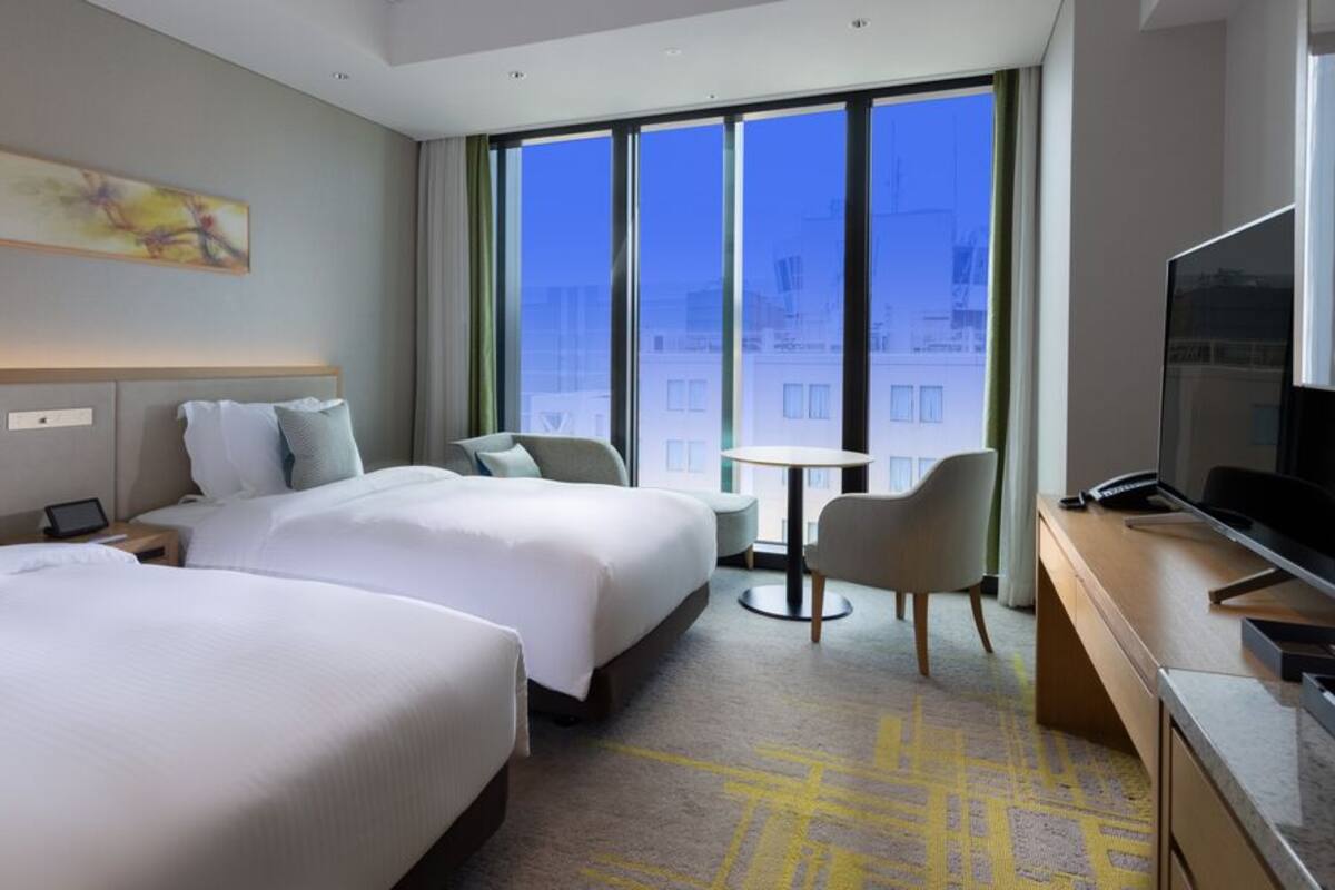 Une chambre d’hôtel avec deux lits, une télévision, une petite table et un balcon avec vue.