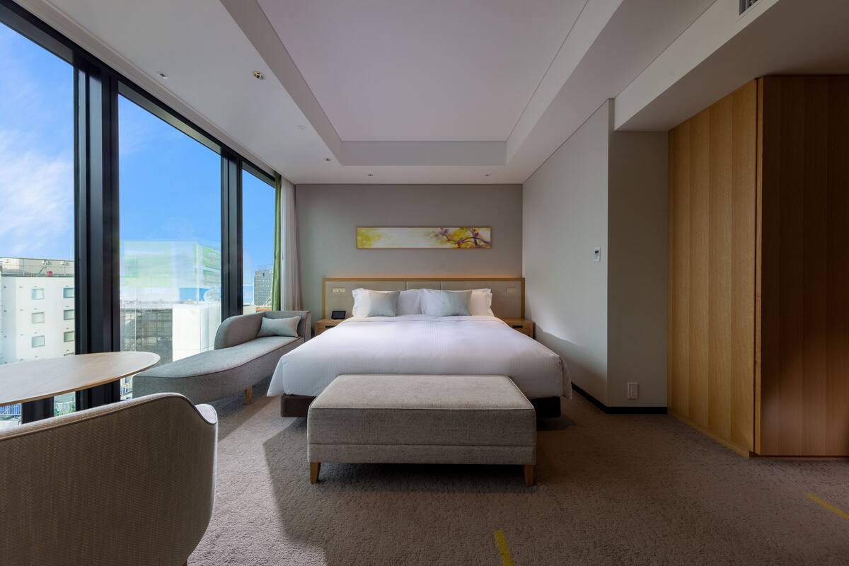 Une chambre d’hôtel moderne dotée d’un grand lit, d’un coin salon, d’un bureau et offrant une vue sur la ville.