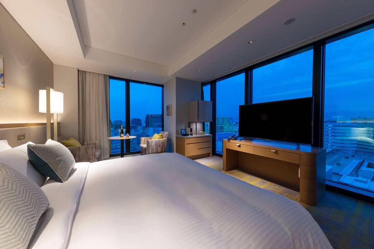 Une chambre d’hôtel moderne dotée d’un grand lit, d’un bureau, d’une télévision et offrant une vue sur la ville.