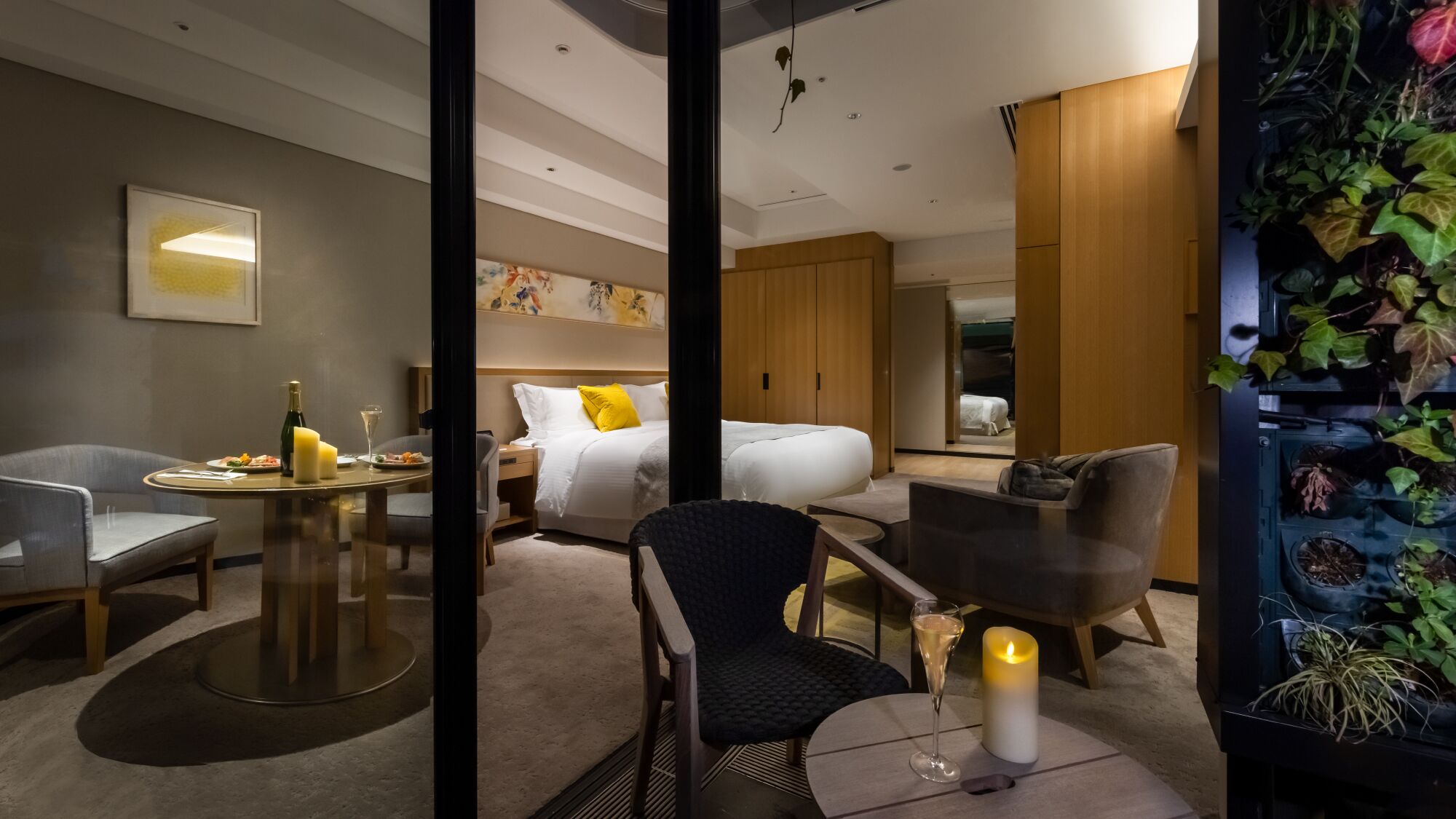 Een hotelkamer met een bed, een eettafel met stoelen, een zithoekje en een wandplank met planten.
