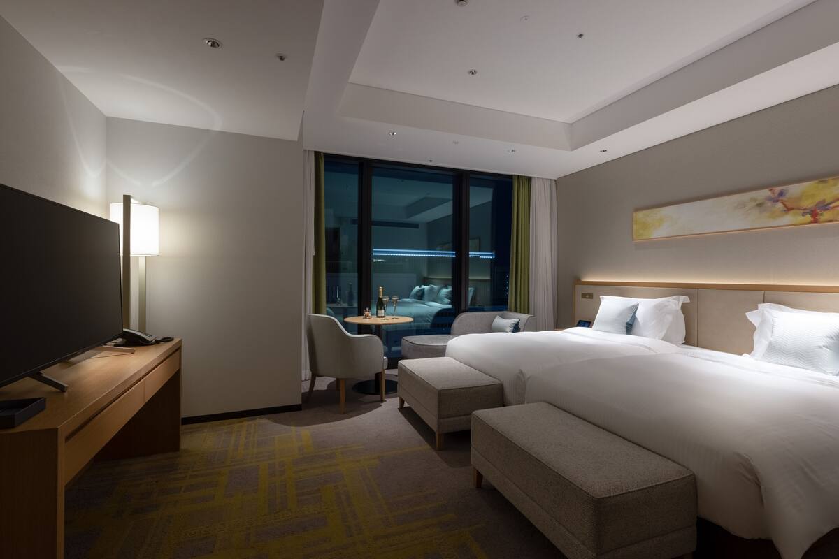 Une chambre d’hôtel avec un lit, un bureau, une chaise, une petite table et un téléviseur.