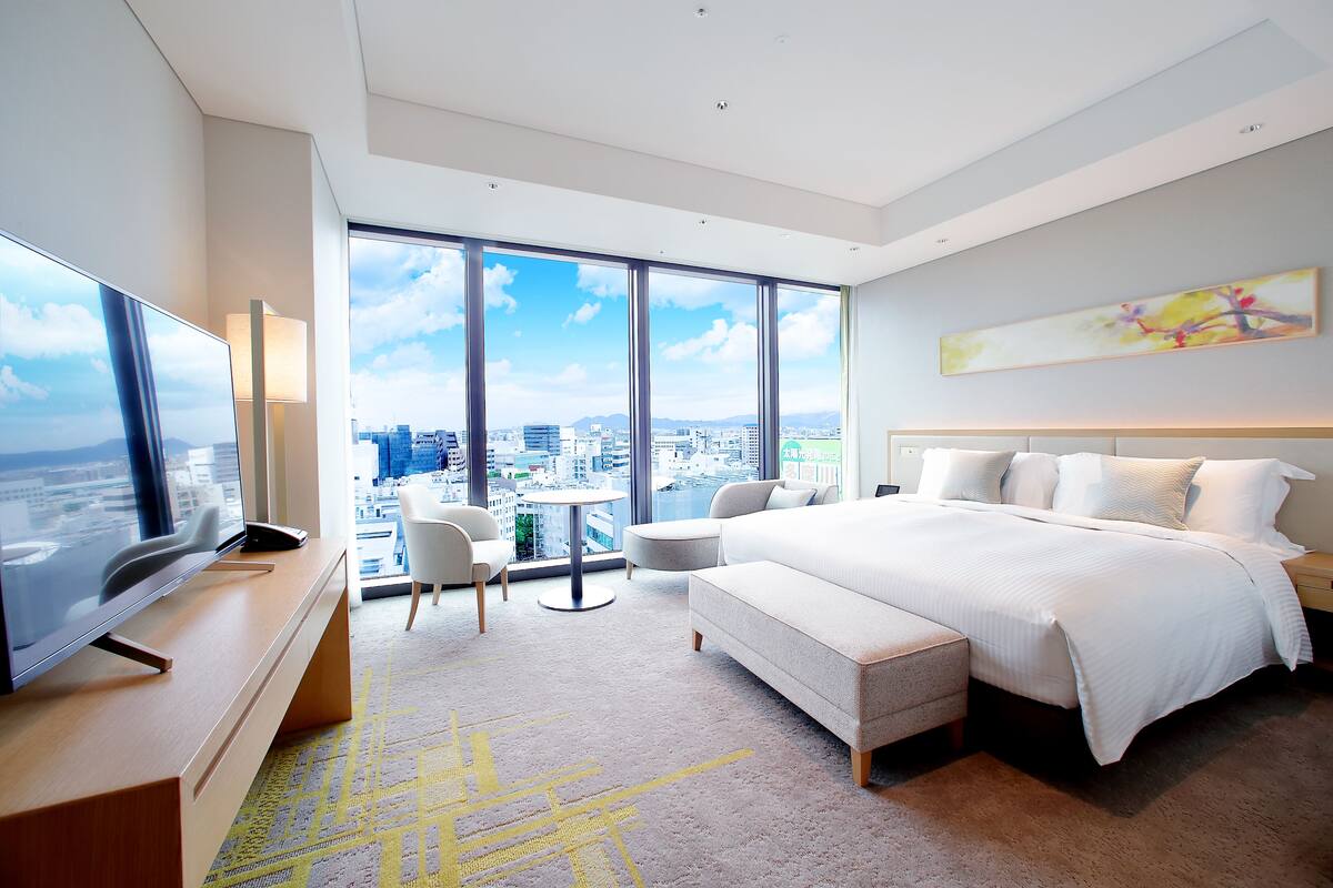 Une chambre d’hôtel moderne dotée d’un grand lit, d’une télévision, d’un bureau et offrant une vue sur la ville grâce à de grandes fenêtres.