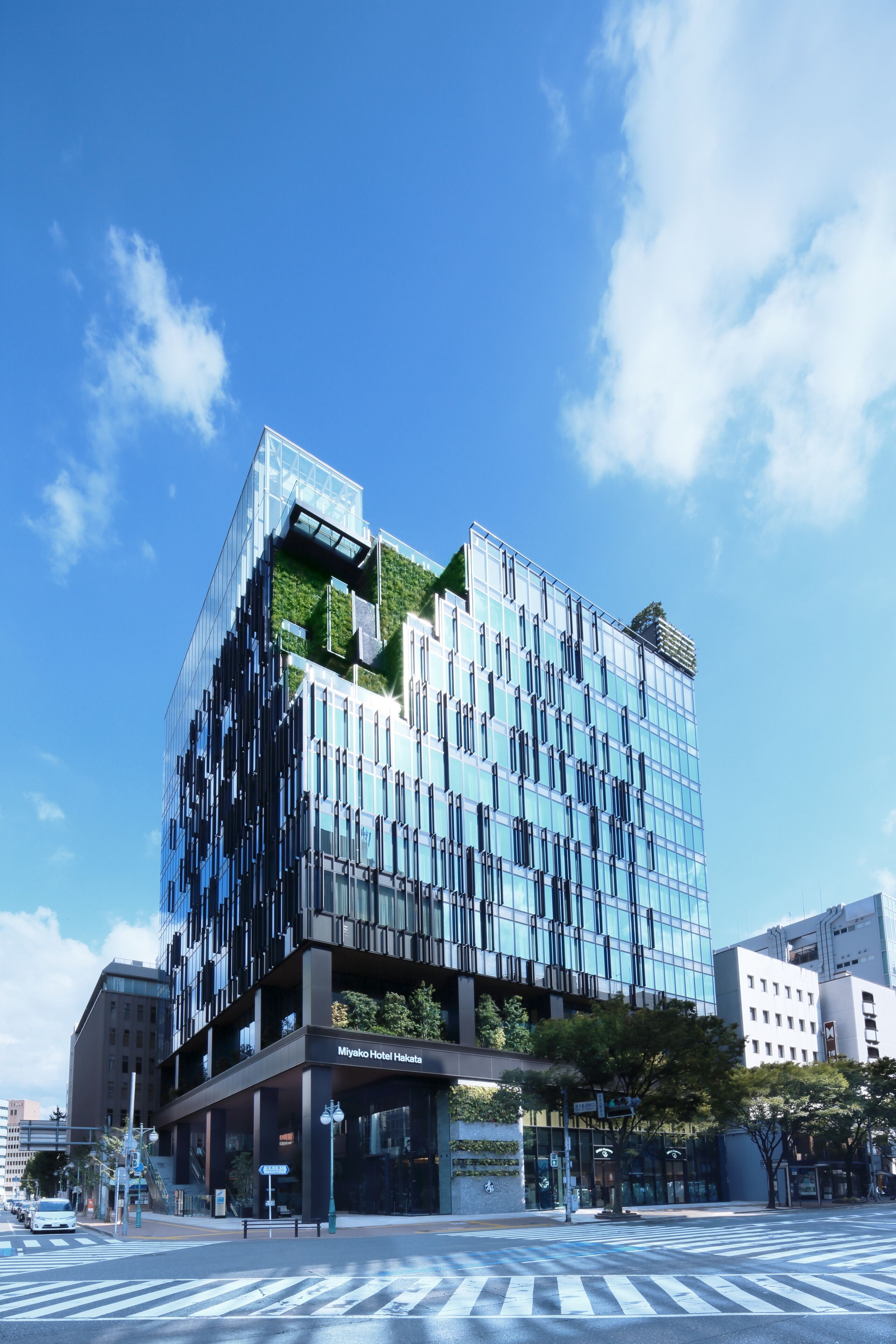 A modern hotel with a unique architectural design, featuring a mix of glass and greenery on the facade, and a clear blue sky in the background.