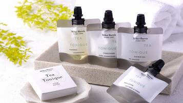 Vier flessen Miller Harris Tea Tonique producten, waaronder shampoo, conditioner, douchegel en bodylotion, gerangschikt op een stenen oppervlak met een witte doos van hetzelfde product.