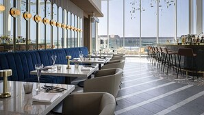 Een modern restaurant met een hoge plafond, grote ramen en een bar.