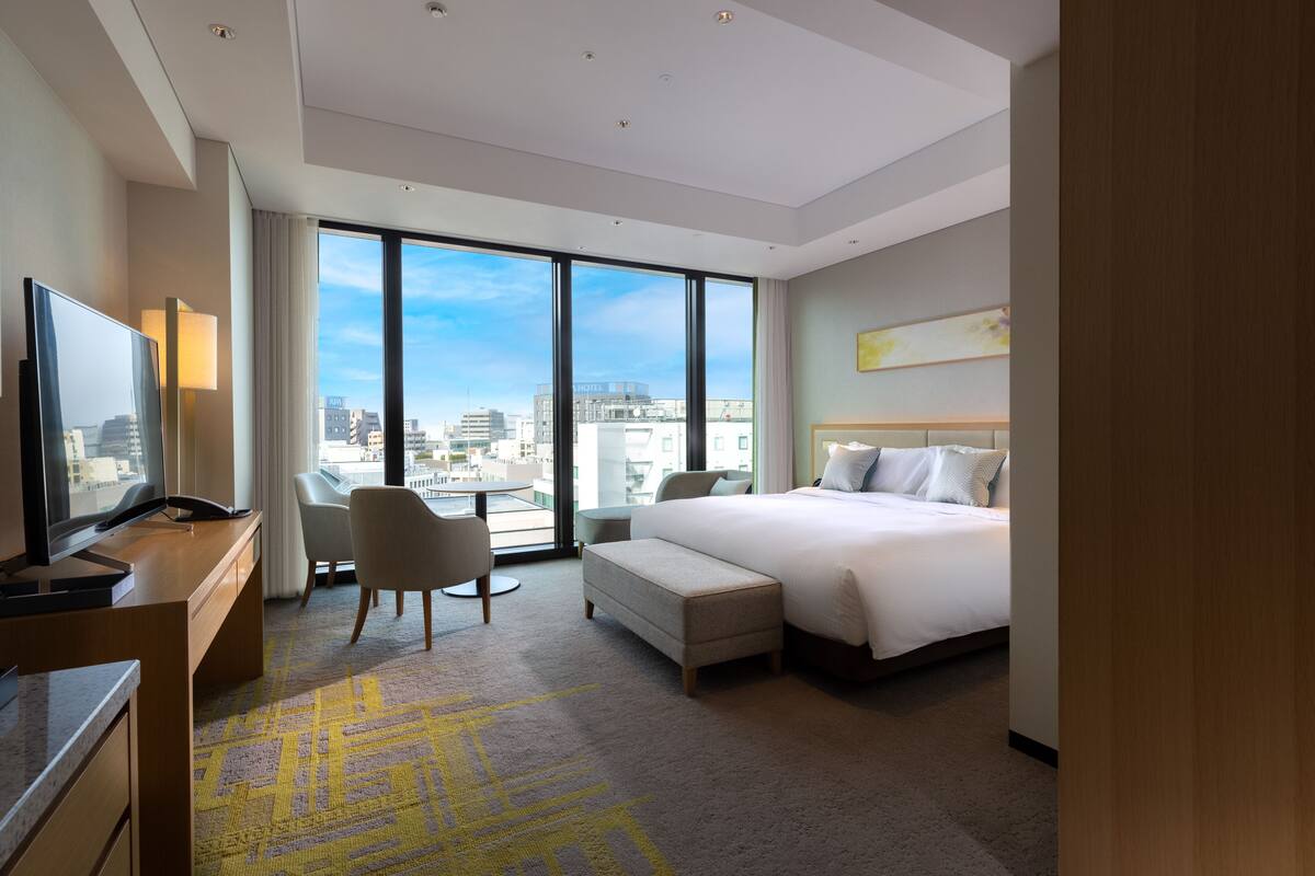 Une chambre d’hôtel moderne dotée d’un grand lit, d’un bureau avec un ordinateur, d’une chaise et offrant une vue sur la ville grâce à de grandes fenêtres.