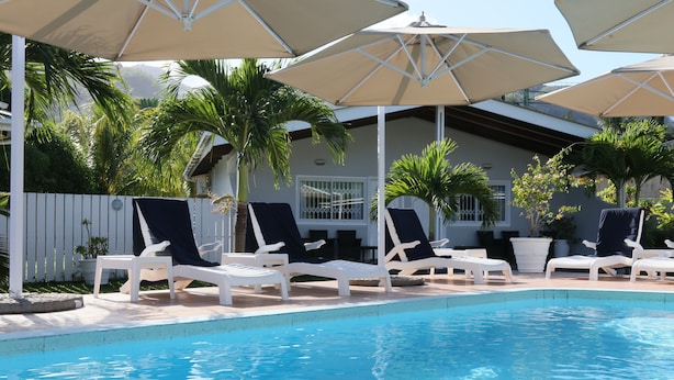 Un espace piscine agrémenté de chaises longues et de parasols, entouré d’une clôture blanche et de palmiers.
