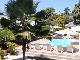 A pool area with lounge chairs and umbrellas, surrounded by palm trees and other tropical plants.