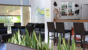 Un hall d'hôtel avec des meubles en osier, un coin bar et une vue sur la verdure environnante.