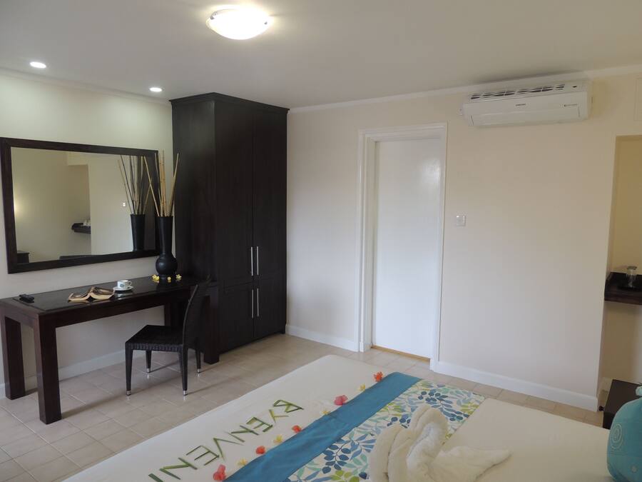 A bedroom with a dark wooden wardrobe, a white door, a desk with a chair, and a bed with a decorative towel.