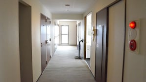 A hallway with doors on both sides, a fire alarm on the right, and a window at the end. - Hotel Maruchu Classico (Tokyo)