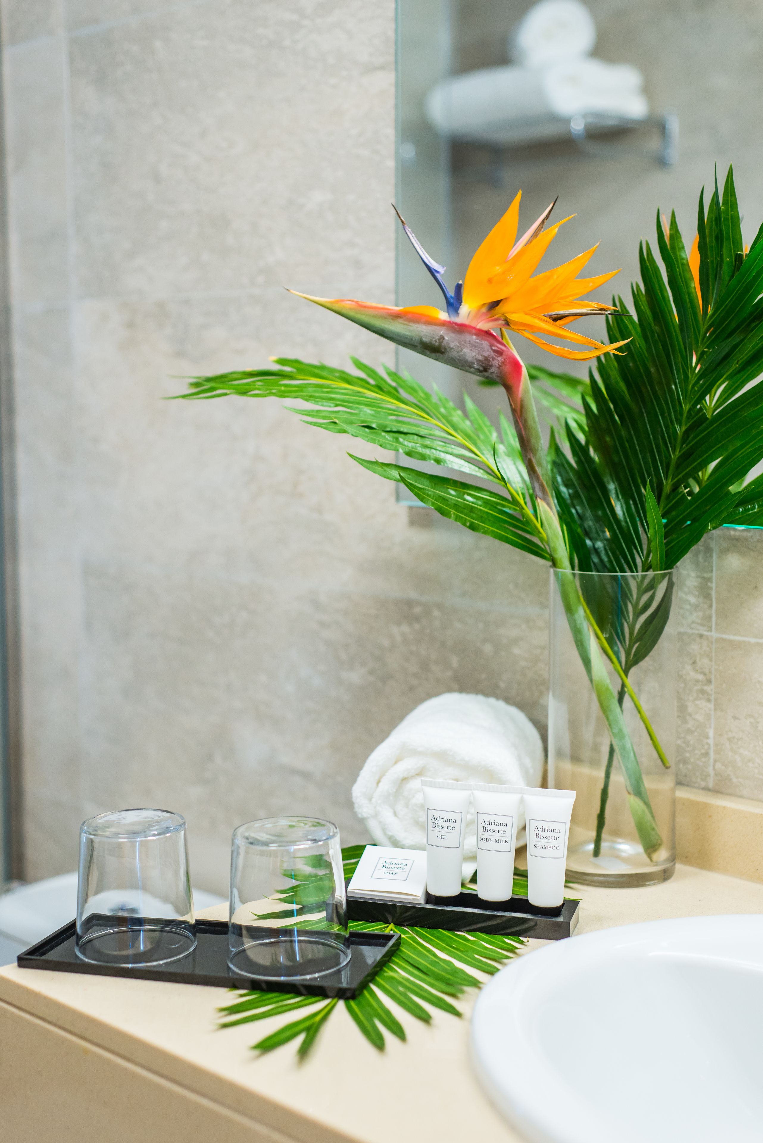 Un baño con un florero de vidrio con una flor de ave del paraíso, una toalla blanca y artículos de aseo en una bandeja.